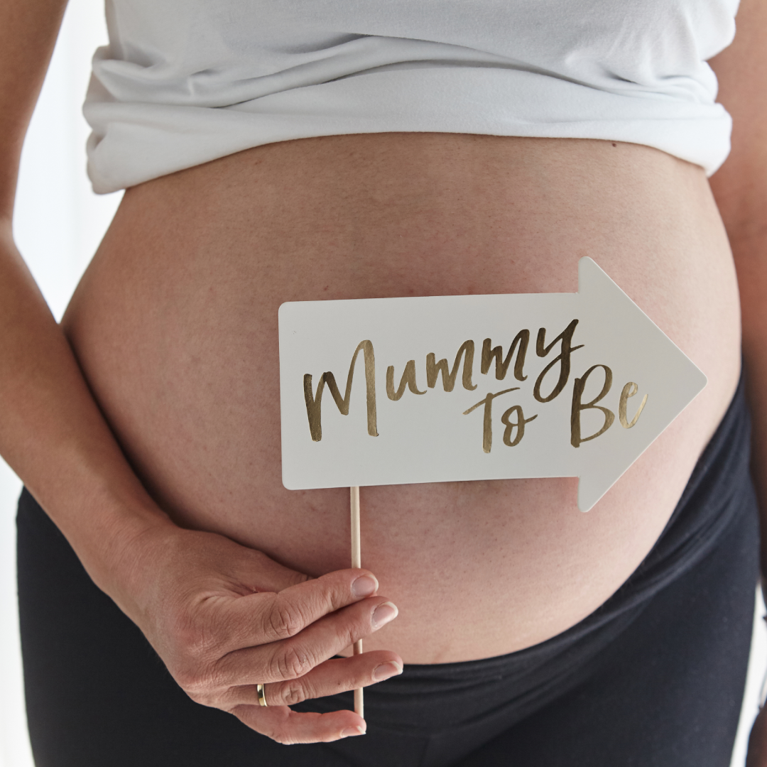 Photo of a pregnant woman, holding an arrow-shaped sign saying "Mummy to Be"