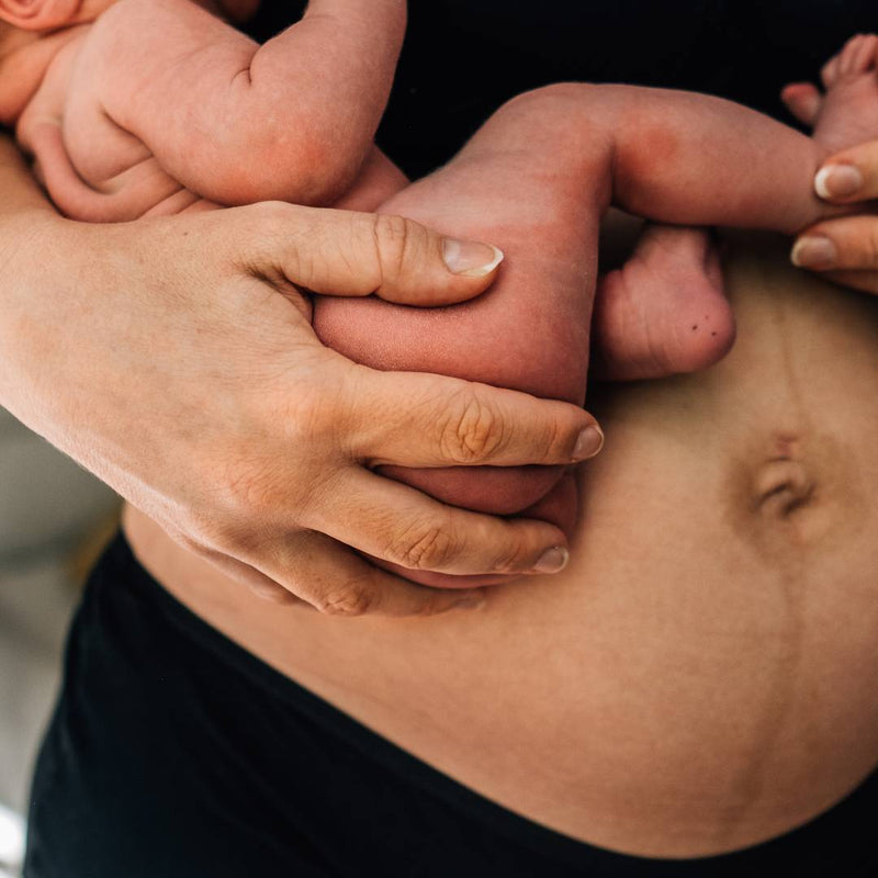 Closeup photo of a mother holding her newborn & showing her postpartum belly